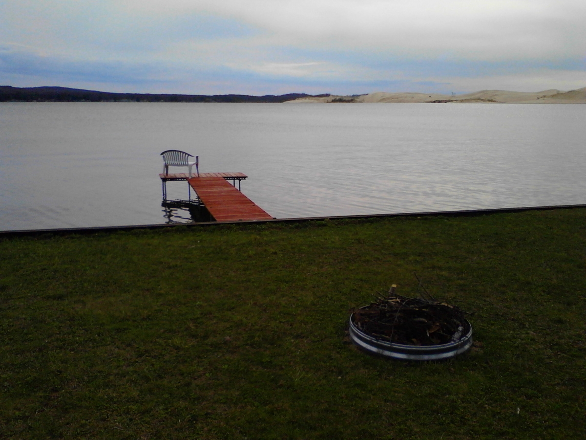 A fire pit in the grass near a dock.