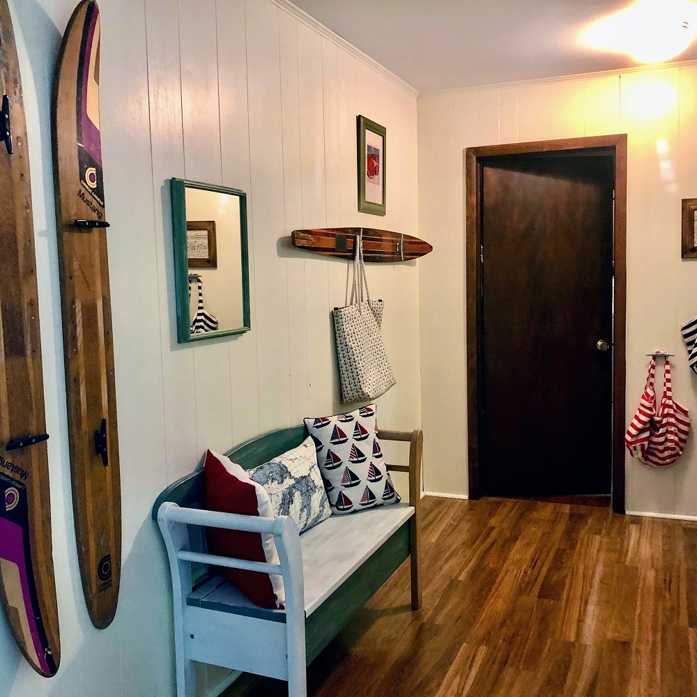 A bench in the corner of a room with two skis hanging on it.