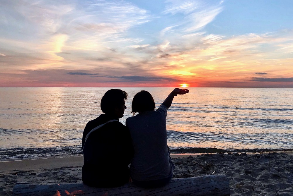 Two people sitting on a beach watching the sunset.