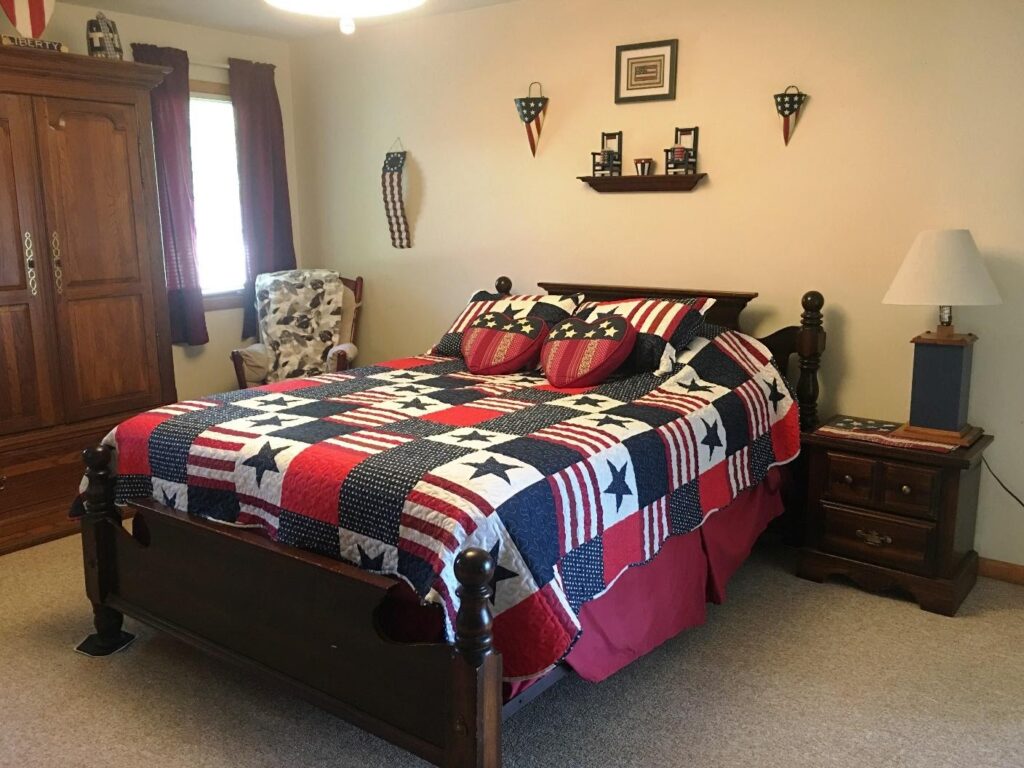 A bedroom with a bed, chair and dresser.