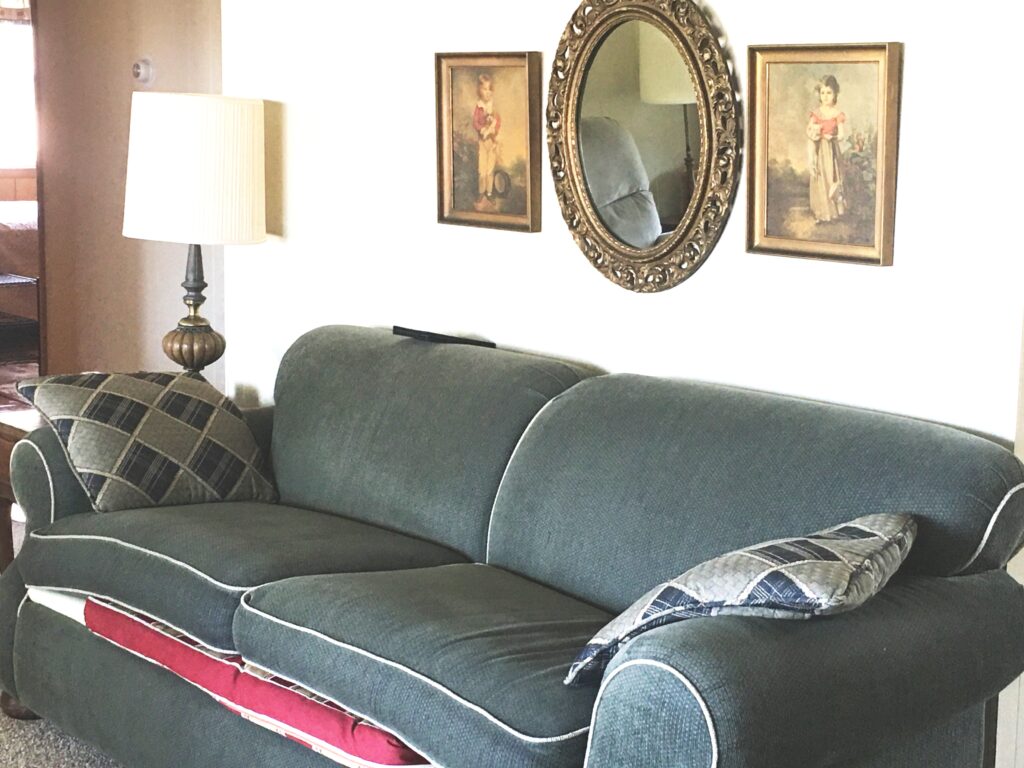 A couch with pillows and a lamp in front of a mirror.