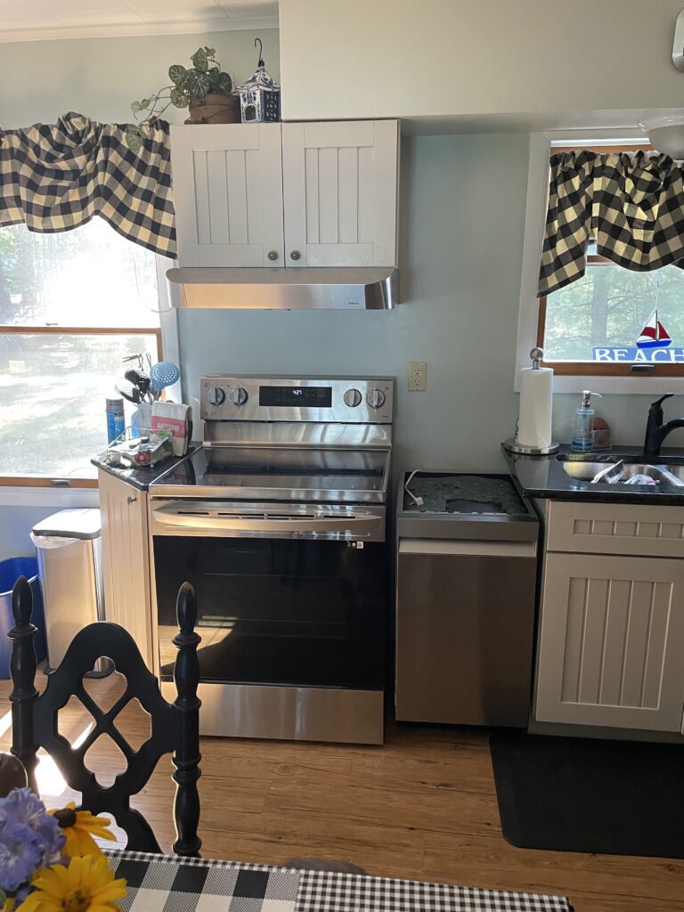 A kitchen with stainless steel appliances and black checkered curtains.