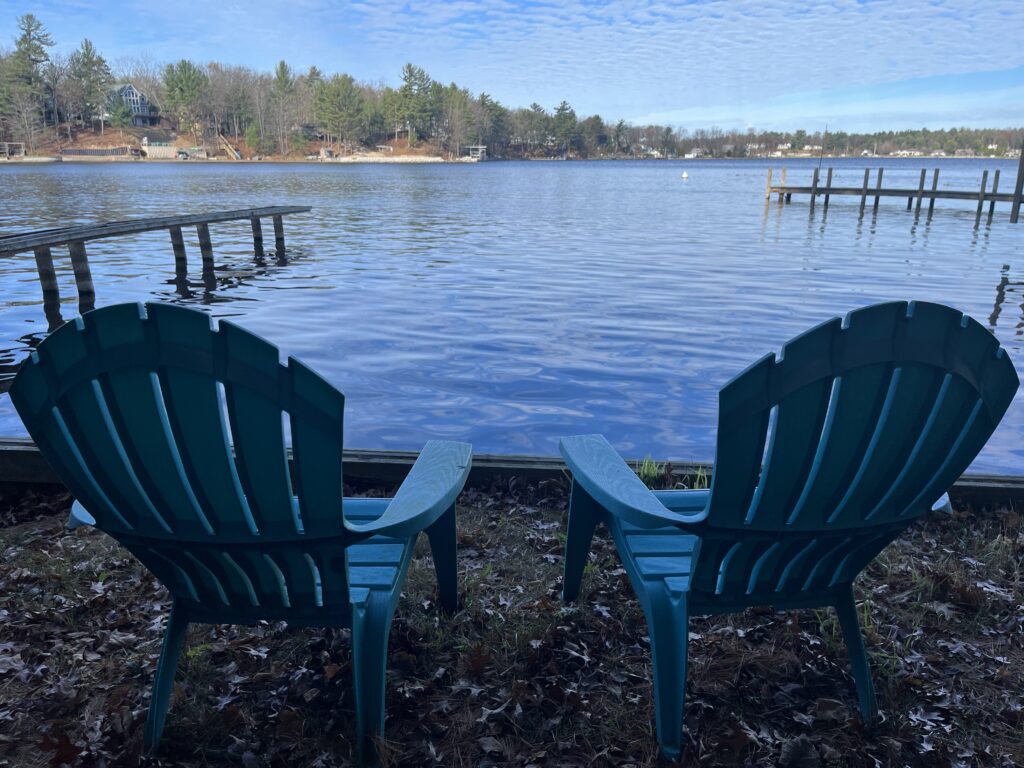 Two lawn chairs sitting on the ground near a body of water.