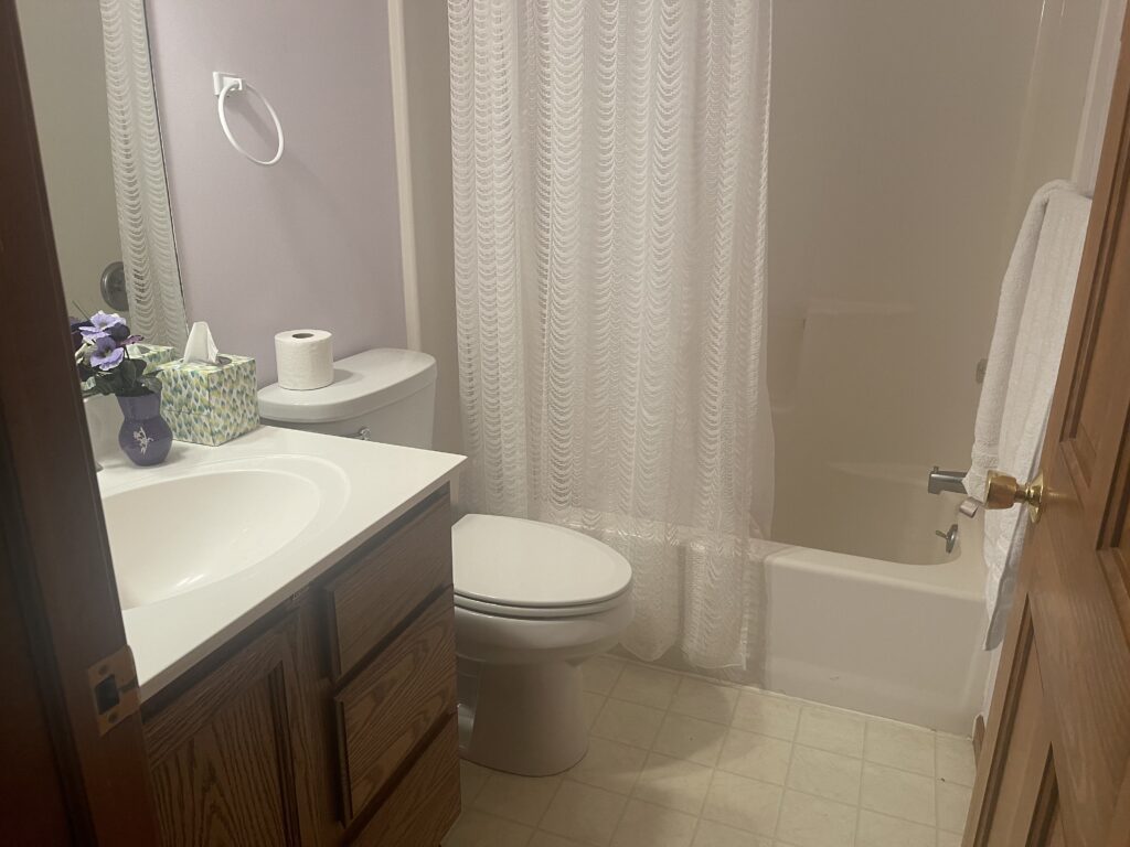 A bathroom with white tile and wood cabinets.